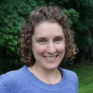 A head shot of a smiling young woman with curly brown hair