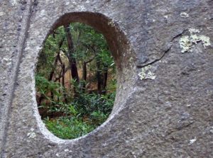 a sone with an imperfect hole through it that looks on a peaceful forest.