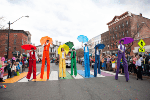 People in rainbow costumes on stilts.