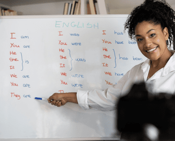 A woman teaching English pronouns and writing on a white board.