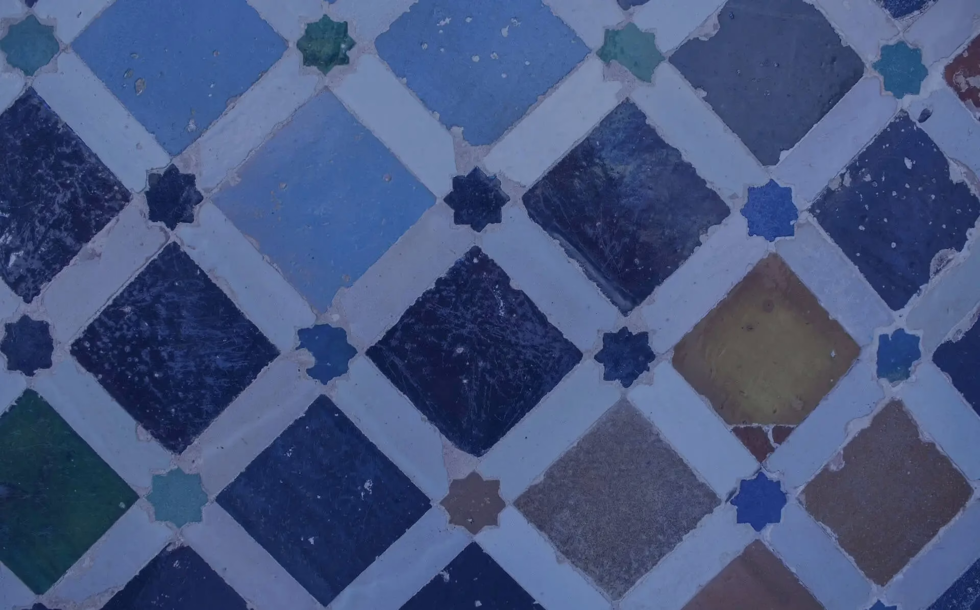 A photograph of beautiful, multicoloured tiles, set in a diamond pattern with eight-sided star tiles placed at the intersections of the different tiles.