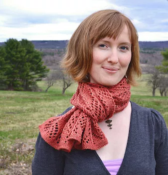 Woman with short red hair, wearing knitted orange scarf outside.