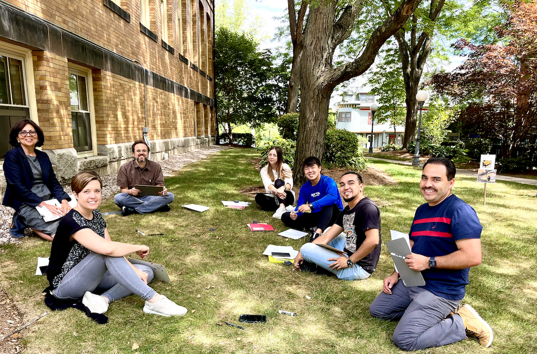 A group of Spanish students enjoying class outside in the shade of a large tree.