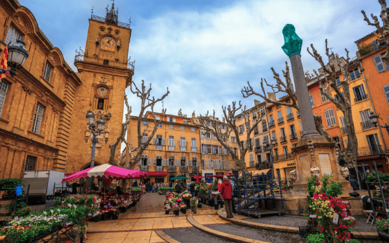 A view of a cathedral in Aix-en-Provence, France with colorful umbrellas over market stalls selling flowers.
