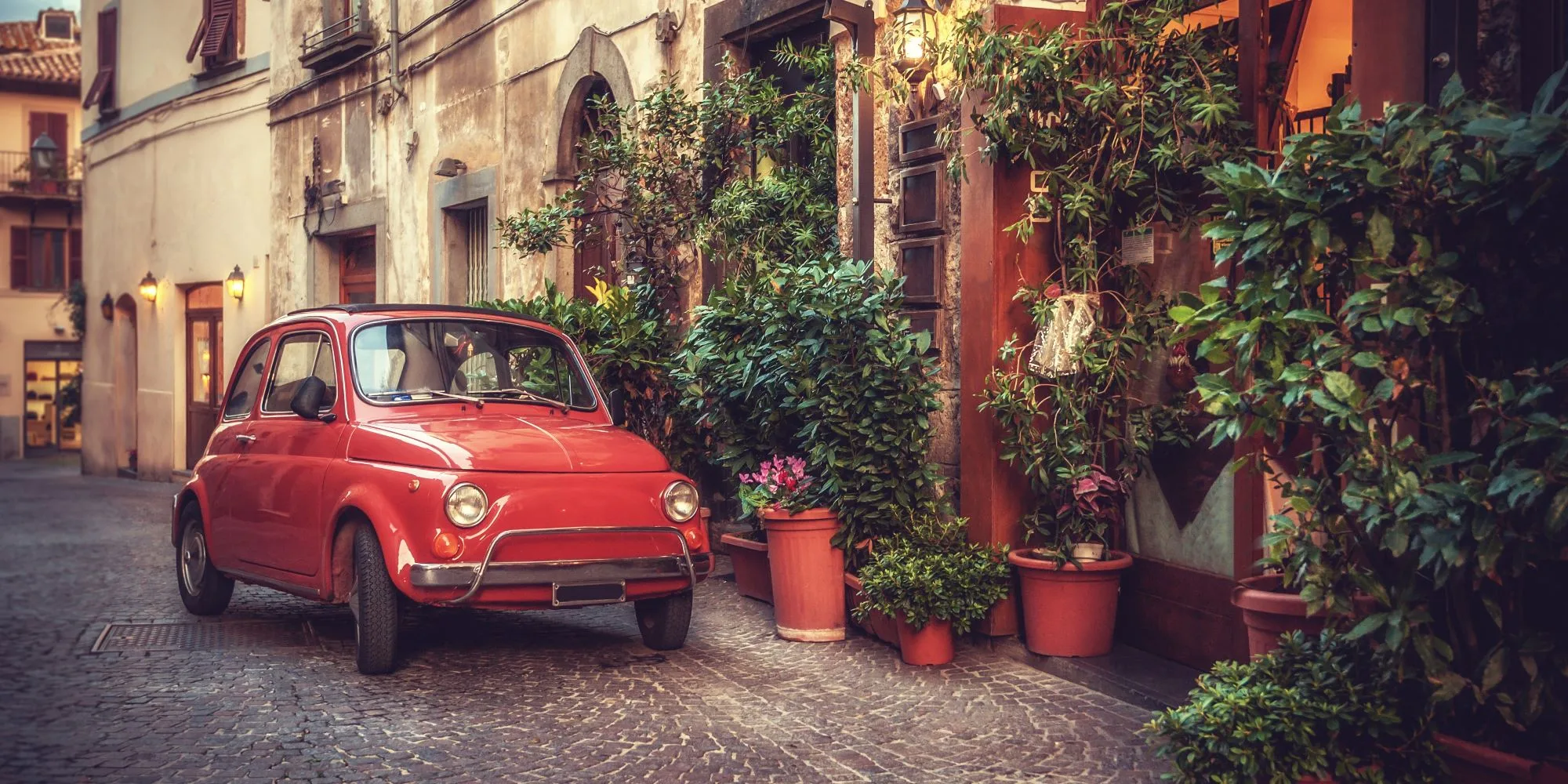 A red fiat on a cobbled street in Italy.