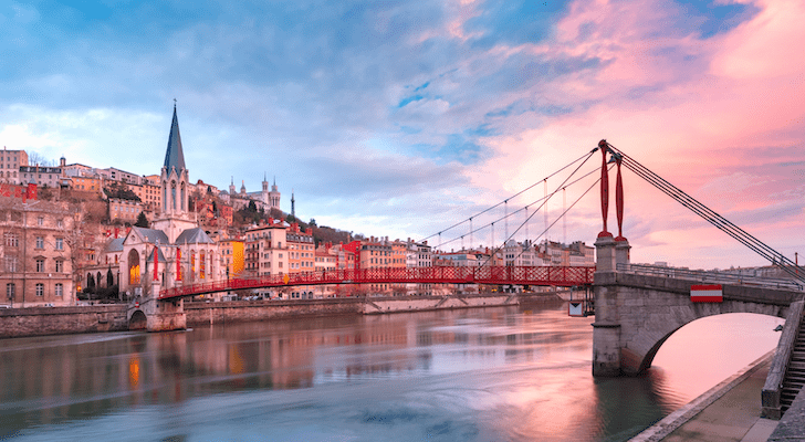 A suspension footbridge across a river with a church in the background at sunset in Lyon, France.