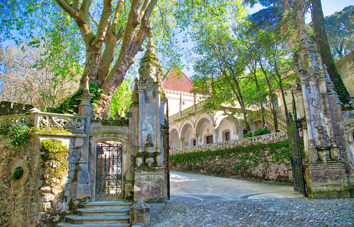 The lichen covered stone pillared and tree shaded entrance and cobblestones drive to the Quinta da Regaleira, a UNESCO World Heritage Site.