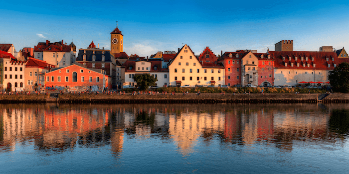 Historic European town with colorful buildings reflecting in the river at sunset.