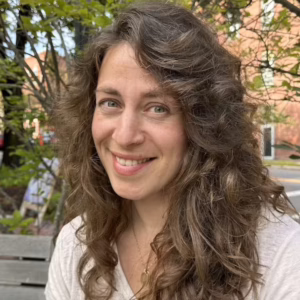 Spanish Instructor, Lianna Hart, sitting on a bench outside on a sunny day smiling.