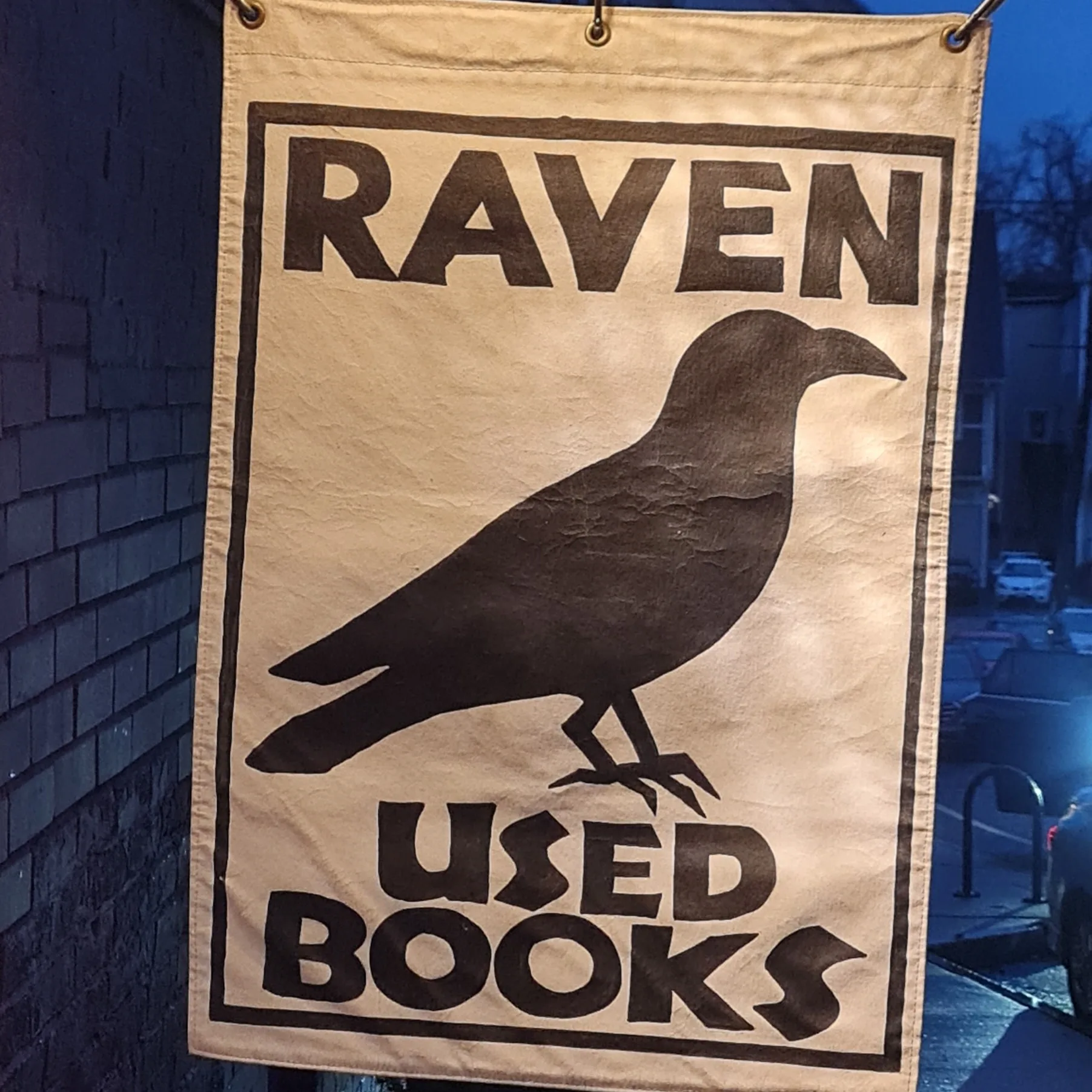 A cloth sign with a clack bird that says Raven Used Books.