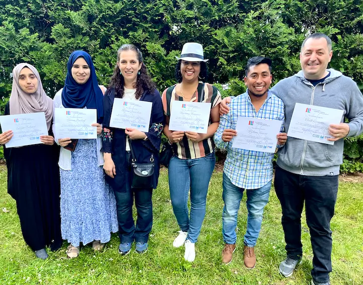 Six adult immigrant ESOL student graduates golding their diplomas.