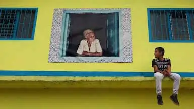 A boy sitting on the ledge of a house looking at a poster of a woman looking at him.