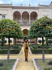 a person standing between 2 orange trees in front of a historic building