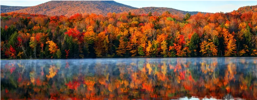A view of the Connecticut River with fall foliage and mountains reflected in the water.