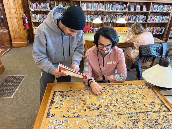 Two people studying a puzzle in a library.