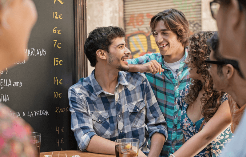 A group of young friends laughing and enjoying drinks together at a lively tapas bar.