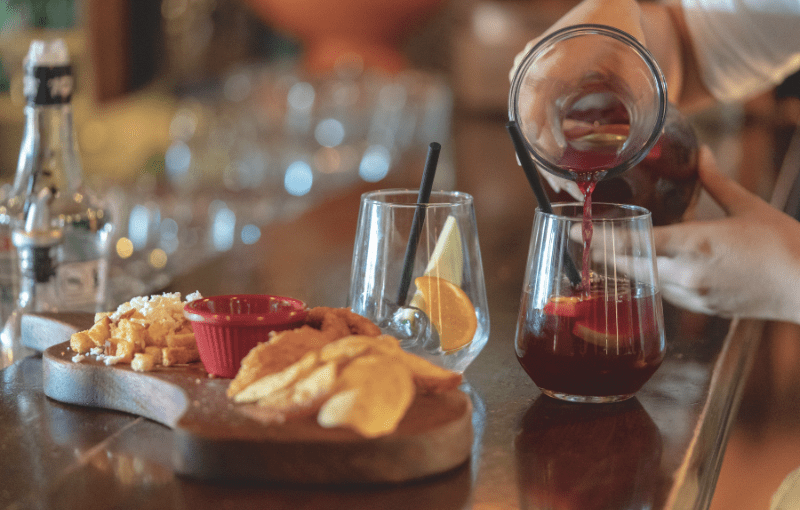 A person pours refreshing sangria into a glass, surrounded by delicious tapas on a table.