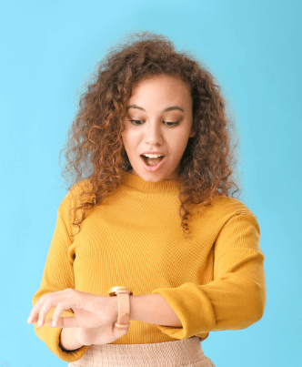 A woman with curly hair gazes at her wrist, checking the time on her watch with a surprised expression.