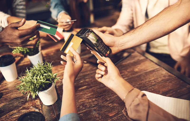 A group of friends at a table, each holding credit cards, ready to split the bill after a fun meal together.