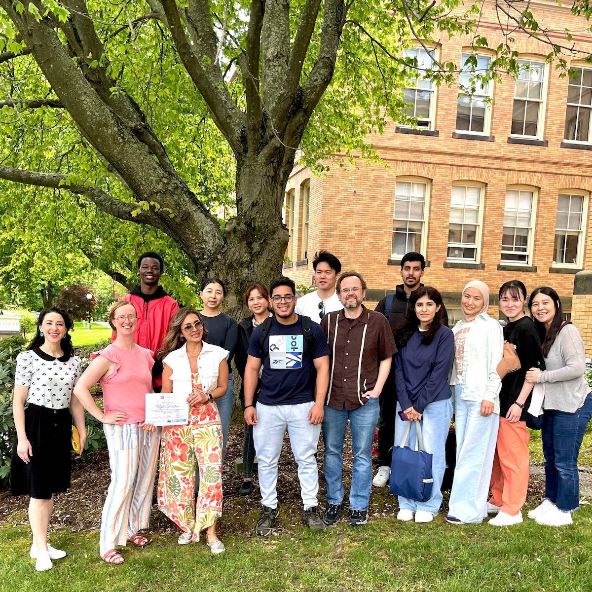 A diverse group of individuals gathered together in front of a large, leafy tree, smiling and enjoying the moment.