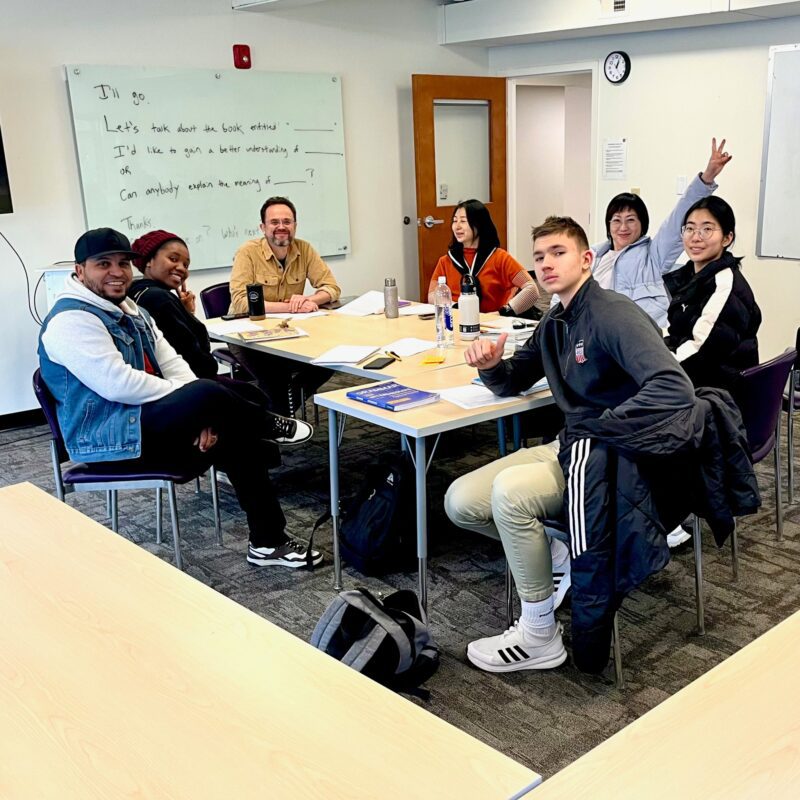 Several people seated at a table, actively participating in a classroom discussion.