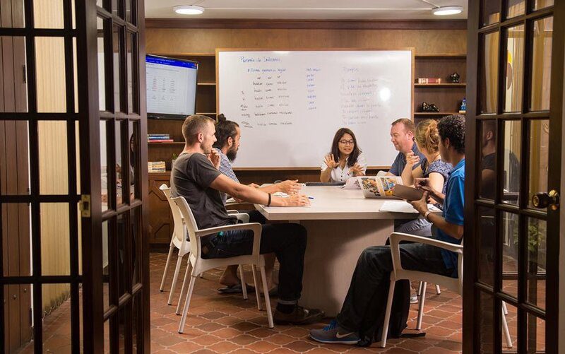 a group of people seated around a table in a classroom engaged in learning.
