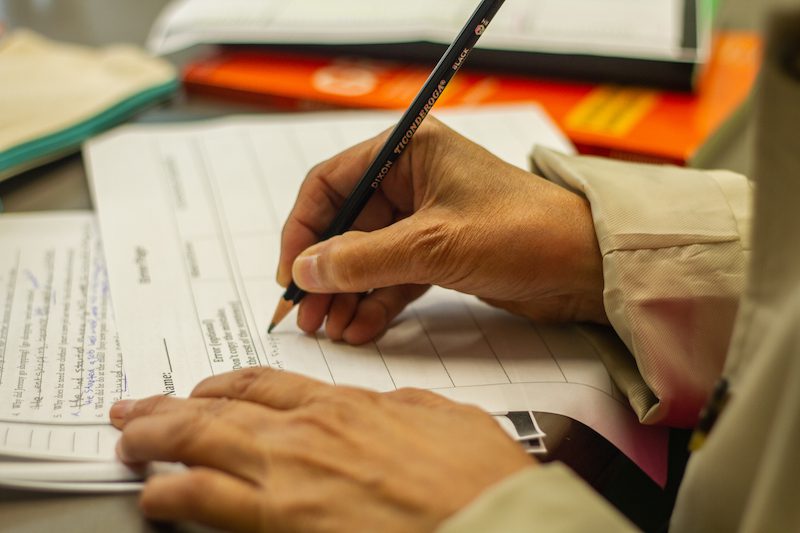 A close-up of a hand holding a pencil, writing on a sheet of paper.