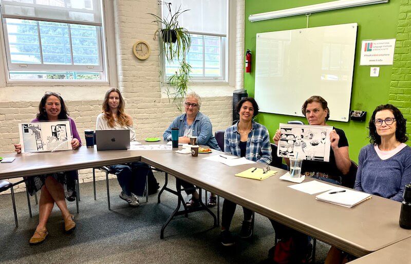 A group of women collaborating at a table, surrounded by papers and laptops, engaged in discussion.