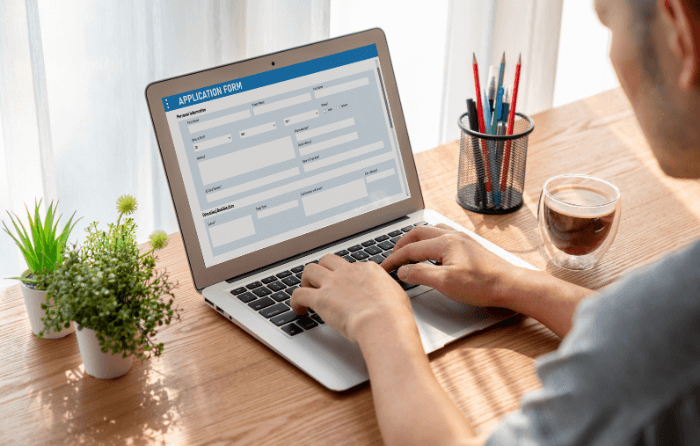 a laptop open on a table with a person filling out an application form.
