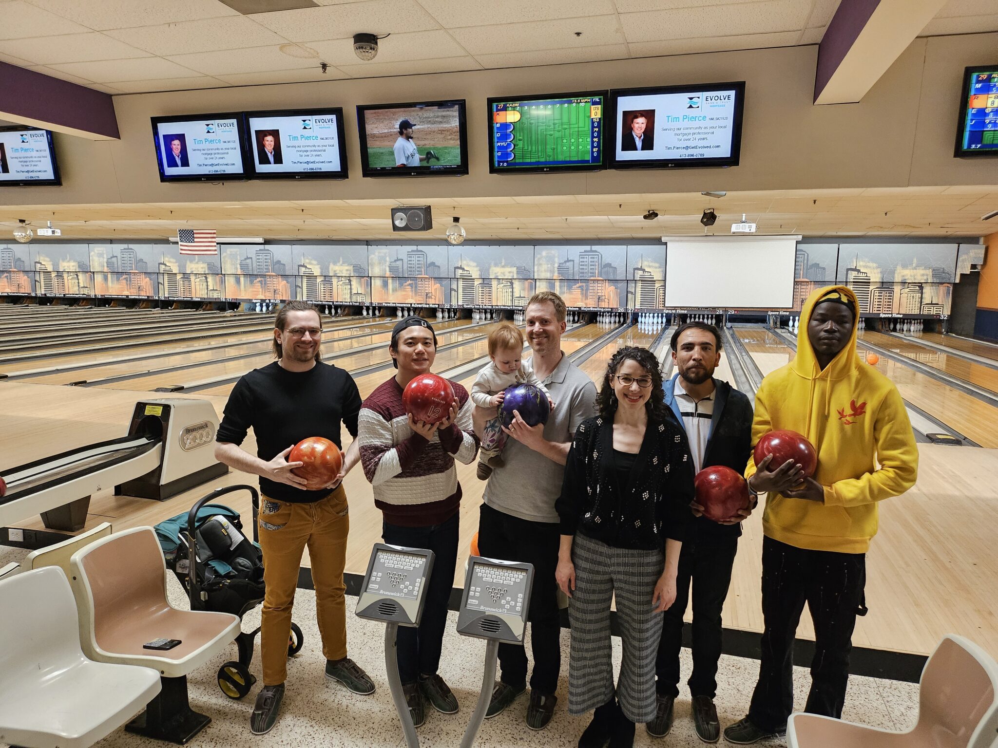Six people and a baby at a bowling alley.