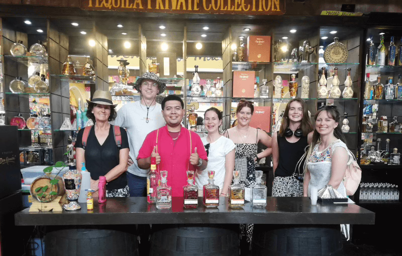 A group of five people smiling and posing together in front of a liquor store entrance.