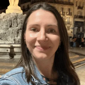 A woman smiling in front of a stone fountain with a statue.